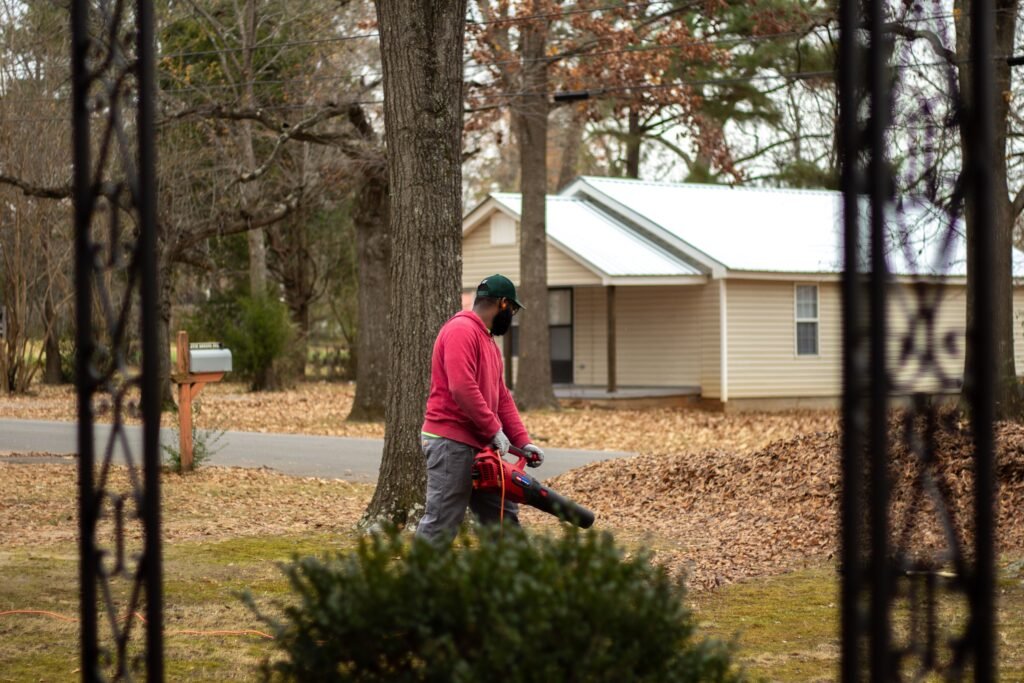 A man cleans fallen leaves with a blower in a residential neighborhood during autumn.