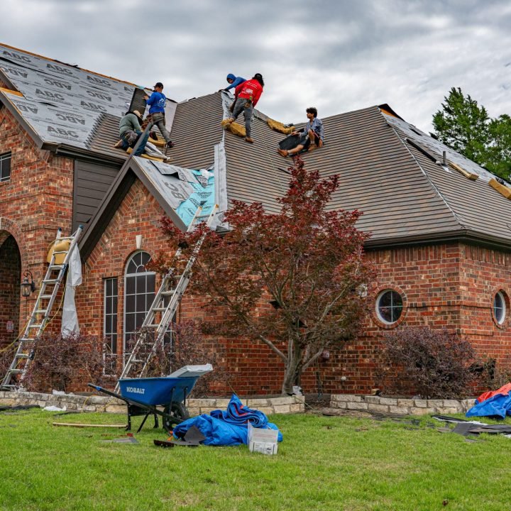 Roofers working on brick home in Allen, Texas, addressing shingles and roofing materials.
